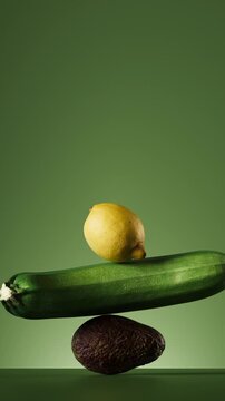 Vertical video of lemon, cucumber, and avocado stacked in a balancing tower, smoothly rolling on each other on green background. Creative food motion graphic for social media.