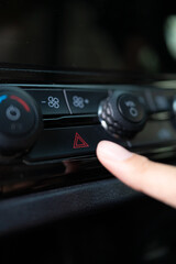 Close-up of a finger pressing the red hazard light button on a car's console. Ideal for themes related to emergency, road safety, car breakdown, and automotive security concepts. Vertical Shot