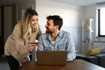 happy couple making an online payment with a credit card and laptop at home, cashless lifestyle