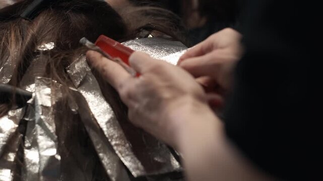 Professional hair colorist with red nails using a red comb to weave and section dark hair over aluminum foil