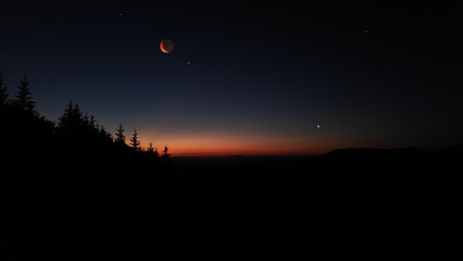 Lunar eclipse, stars and planets above landscape silhouettes. © astrosystem