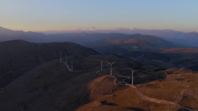 Aerial view of windmills standing tall on the mountain ridge, basking in the warm glow of sunset, Cocullo, Abruzzo, Italy.
