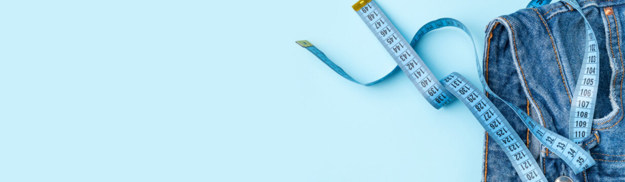 Weight loss and diet concepts. Tape measure instead of belt on blue jeans flat lay top view. Healthy lifestyle, sports and fitness. Overweight or anorexia. Free space for text. Long banner