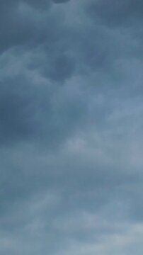 Vertical time lapse of dark storm clouds moving across a moody grey sky. Dramatic atmosphere before rain, overcast weather and nature background.