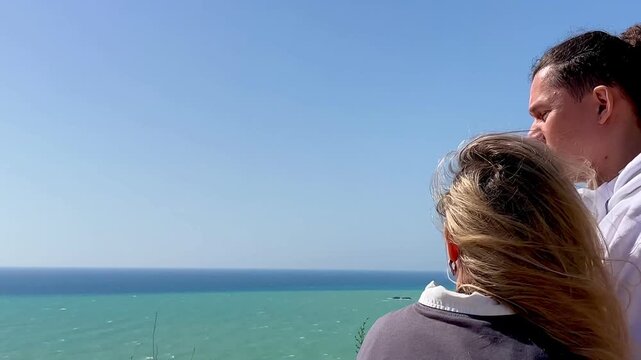 Back view of a hugging couple admiring the Mediterranean Sea from a wooden viewpoint overlooking the white cliffs of Scala dei Turchi in Sicily. Romantic intimate moment symbolizing love, connection.