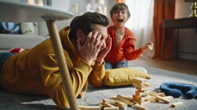 Father ruined jenga tower playing with happy little boy lying home floor closeup