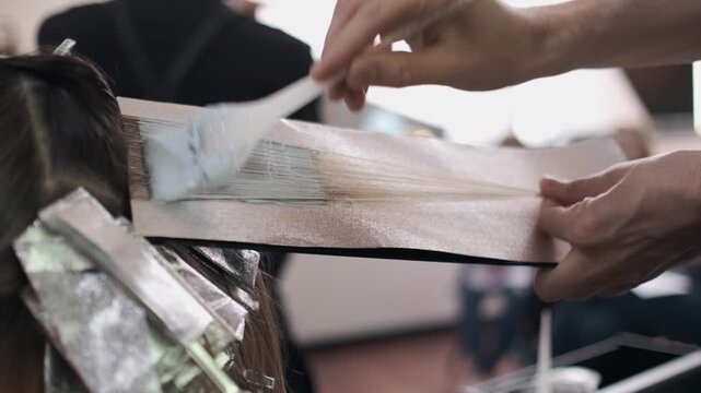 Hairdresser holding a thin section of hair against a foil sheet during a coloring or highlighting treatment in a salon