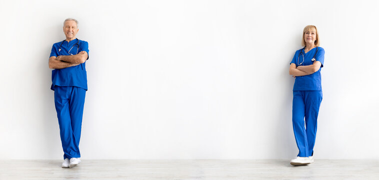 Senior male and female doctors wearing blue scrubs standing with arms crossed against white studio background , symbolizing confidence, professional healthcare teamwork and medical experience