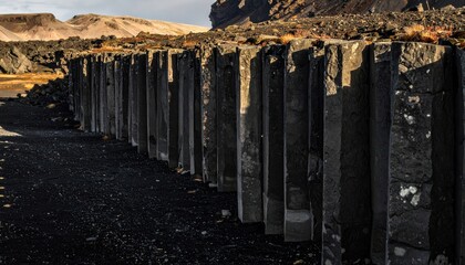 Imposing formation of dark basalt columns arranged in a rigid, geometric natural structure against a rocky landscape