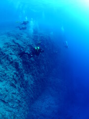 scuba divers around a reef underwater deep blue water big rocks  air bubbles rising