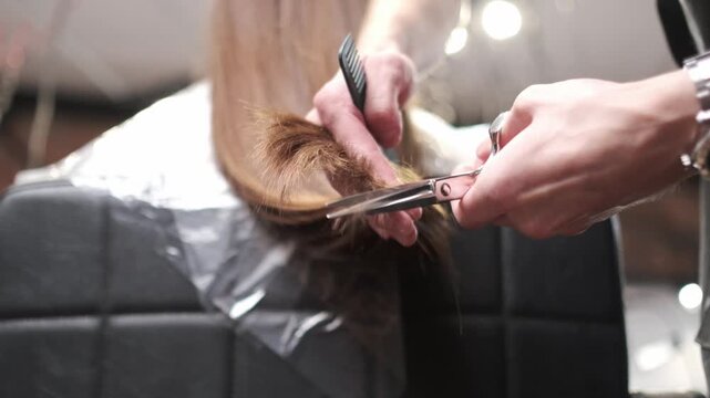 Professional hairstylist using scissors and a comb to trim the ends of a client's long brown hair in a salon