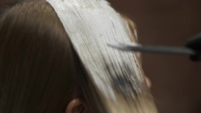 Hairstylist applying white dye mixture to hair roots with a tint brush in a salon