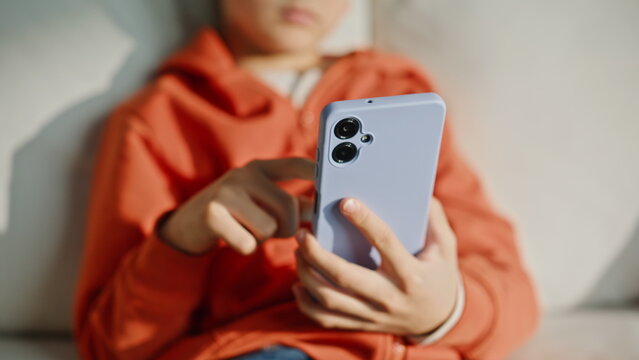 Kid hands scrolling mobile phone news feed sitting living room couch closeup. 