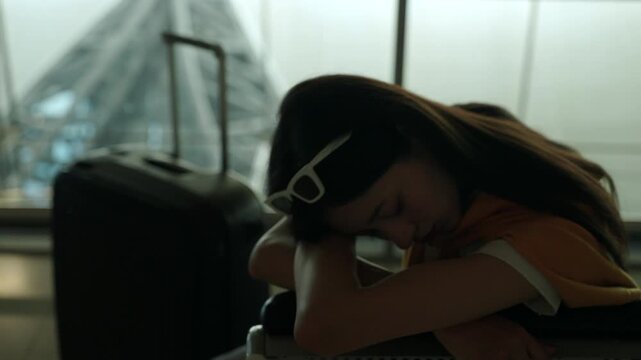 Tired young sola woman traveler sleeping on airport waiting chairs while holding smartphone and boarding pass after long flight delay, bored passenger waiting at airport terminal.
