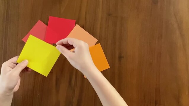Child placing the fifth small origami paper into a colorful arrangement, slow motion