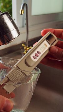 Vertical video. First Person View Of Hand Measuring Drinking Water With Digital Tester Showing High Ppm Result In Glass Near Kitchen Sink. Water Quality Concern And Rechecking