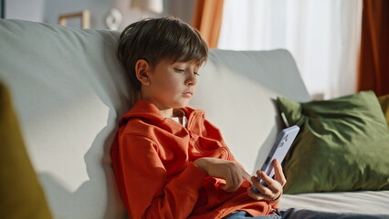 Relaxed boy browsing cellphone sitting home sofa closeup. Child scrolling phone