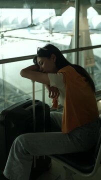 Tired young sola woman traveler sleeping on airport waiting chairs while holding smartphone and boarding pass after long flight delay, bored passenger waiting at airport terminal.
