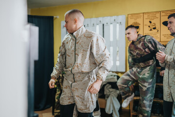 Fototapeta premium A soldier in desert camouflage jacket leads a training drill indoors. Other soldiers in camouflage observe and adjust gear during the scene.