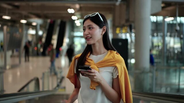 Woman solo traveler stand on escalator at the airport  holding smartphone, passport and boarding pass ready for vacation. Travel lifestyle, digital travel planning and travel insurance concept.
