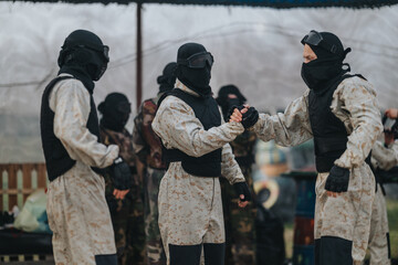 Fototapeta premium Team members in protective vests greet each other on a paintball field, signaling sportsmanship and teamwork after a round.
