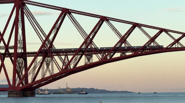 Train crossing historic Forth Bridge cantilever railway at golden hour, Edinburgh, Scotland