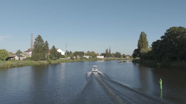 Motorboat cruising on Elbe river with pedestrian bridge in summer, Czech Republic
