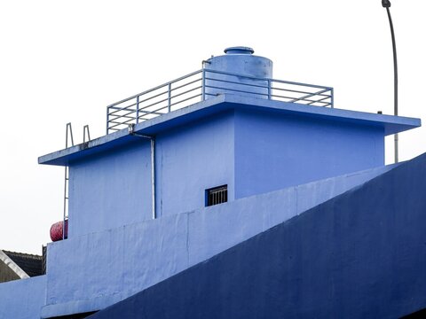 A minimalist shot of a bright blue industrial rooftop featuring a large water storage tank, safety railings, and clean geometric lines against a pale sky.