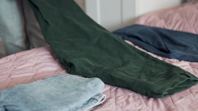 Woman folding denim jeans and stacking them on bed.