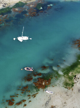 Aerial view of boats resting in the tranquil, turquoise waters, amidst the rugged coastline's embrace, Manche, Normandy, France.