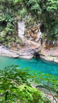 The vertical panning video shows the forest and river flowing through Taroko National Park, Taiwan. Crystal-clear blue water cascades over moss-covered rocks in the valleys.