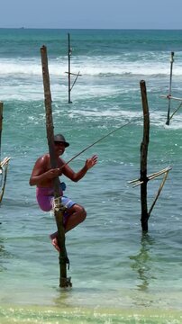 Ahangama, Sri Lanka - 26 March 2024: Horizontal video of fishermen fishing from wooden stilts in the middle of the sea off Sri Lanka. It's a sunny day with strong waves crashing against the shore.