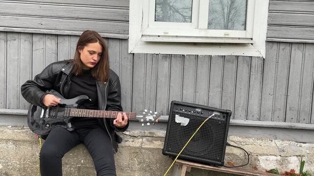 female rock musician in a leather jacket plays an electric guitar with an amplifier