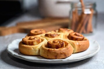 A plate of cinnamon rolls is presented on a gray surface with a jar of cinnamon.