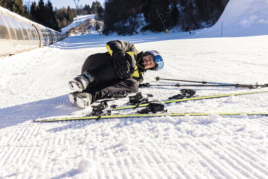 Young sportsman rubbing his hit knee after crash in snow during ski training. Fallen skier holding by his leg.