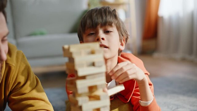 Son building jenga tower putting wooden block on top with happy father closeup.