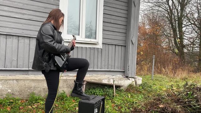 female rock musician in a leather jacket plays an electric guitar with an amplifier