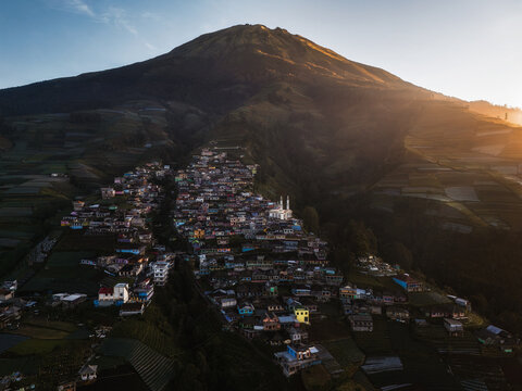 Aerial view of a village nestled at the foot of a majestic mountain, with a white mosque standing out among the clustered buildings, Nepal van Java, Jawa Tengah, Indonesia.