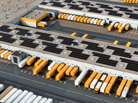 Aerial view of rows of trucks parked at loading docks, solar panels adorning rooftops, reflecting a modern industrial landscape, North Rhine-Westphalia, Germany.