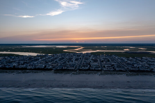 Aerial view of the beach meeting the town under a sky streaked with sunset hues, the wetlands beyond reflecting the fading light, Sea Isle City, New Jersey, United States.
