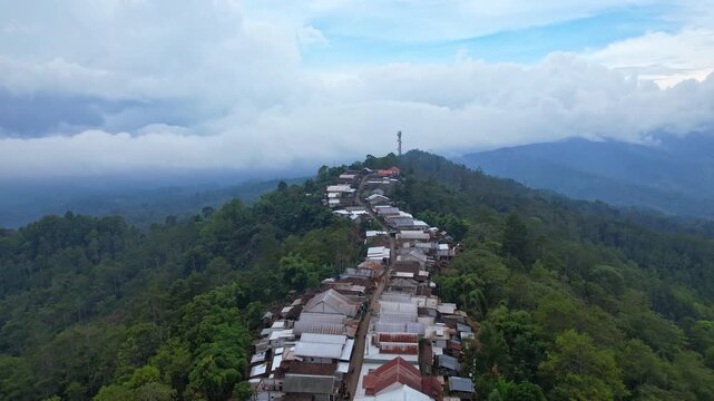 Aerial drone footage of a local village on top of a mountain, with a long main unique road, in a cloudy atmosphere, in Bondowoso regency, Ijen Geopark, East Java island, Indonesia