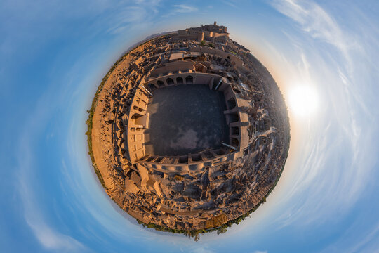 Aerial view of the ancient Arg-e Bam citadel, a sprawling complex of mud-brick buildings under the bright sun, casting long shadows across the arid landscape, Bam, Kerman Province, Iran.