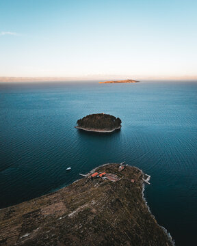 Aerial view of the Isla del Sol, with its rugged terrain meeting the tranquil waters of Lake Titicaca under a serene sky, Copacabana, La Paz Department, Bolivia.