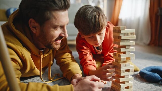 Parent child enjoy jenga building wooden tower lying floor living room closeup. 