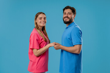 Obraz premium Happy couple stands on blue, holding hands, look into camera. Romantic feelings.