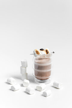 Hot cocoa chocolate drink in a transparent double wall glass with toasted marshmallows on top as a garnish, on white background 