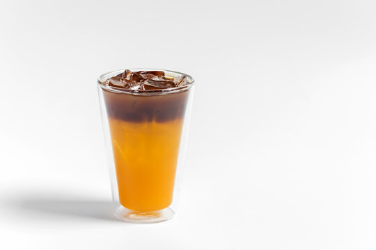 Refreshing bumble orange citrus juice and black coffee espresso drink with ice in a transparent double wall glass on white background 