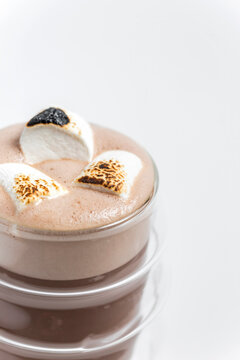 Hot cocoa chocolate drink in a transparent double wall glass with toasted marshmallows on top as a garnish, on white background 