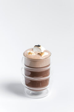 Hot cocoa chocolate drink in a transparent double wall glass with toasted marshmallows on top as a garnish, on white background 