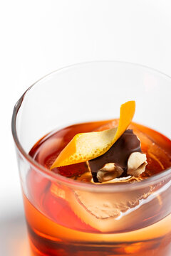 Old fashioned alcoholic cocktail in rocks glass with ice cube, orange twist and a piece of chocolate with hazelnut garnish on white background 
